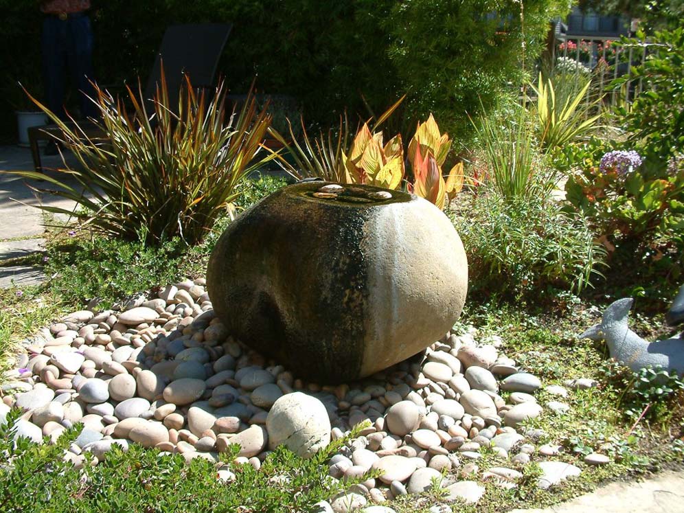 A bubbling sphere water feature in a garden setting.